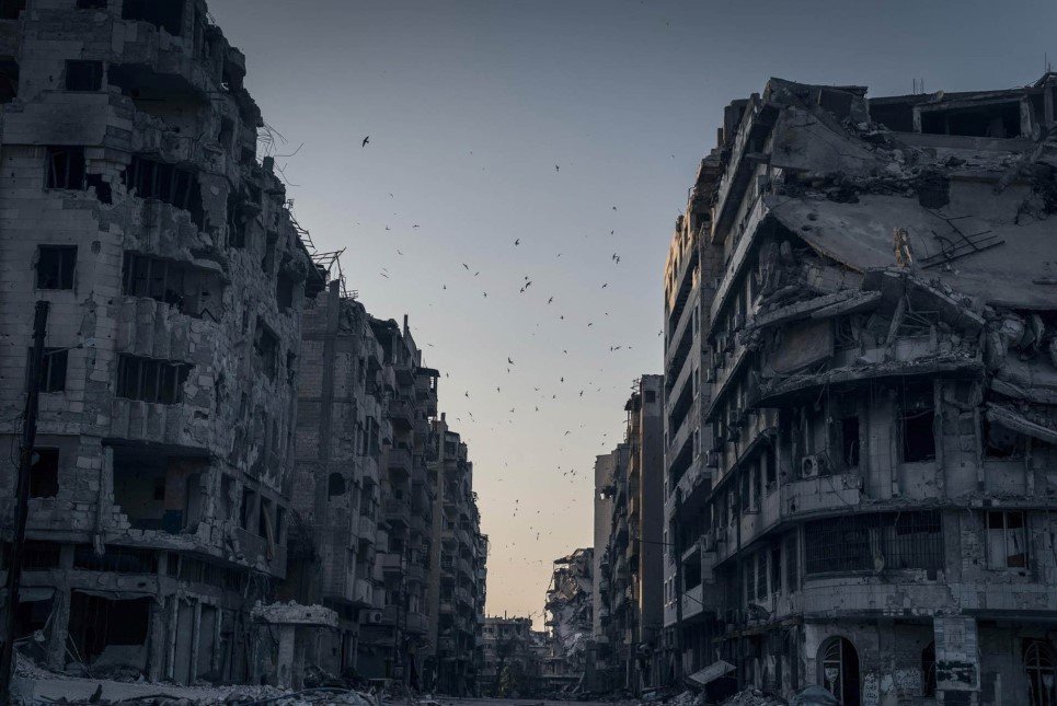 Birds fly over the destroyed houses in Khalidiya district in Homs, Syria. In the vast stillness of the destroyed city center of Homs, there are large areas where nothing moves. Then, suddenly, wind blows a ripped awning, or birds fly overhead.