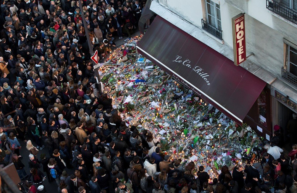 A large crowd gathers to lay flowers and candles in front of the Carillon restaurant after the Paris attacks – Nov. 15, 2015.