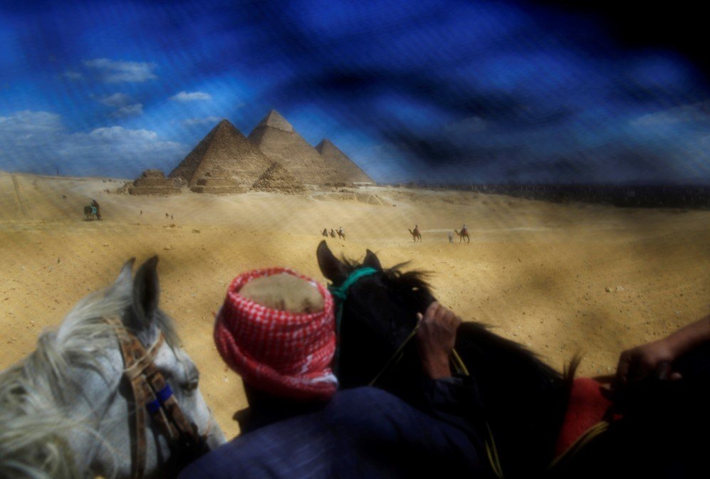 As seen through the veil: A man leading tourists riding horses at the historical site of the Giza Pyramids near Cairo.